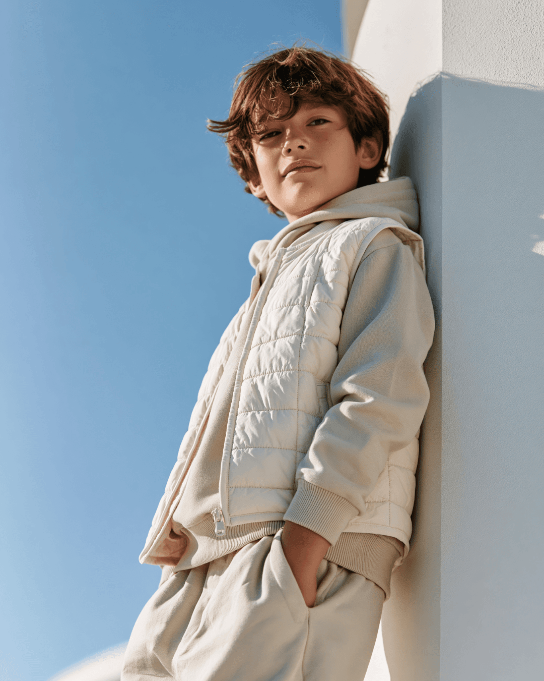 Boy in a cream quilted vest leaning against a wall